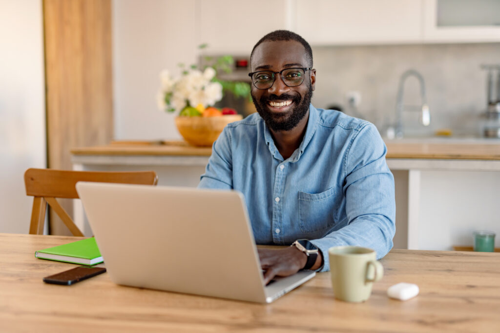 Smiling healthcare professional working remotely from home on a laptop in a bright, welcoming home environment, representing supportive healthcare career opportunities.
