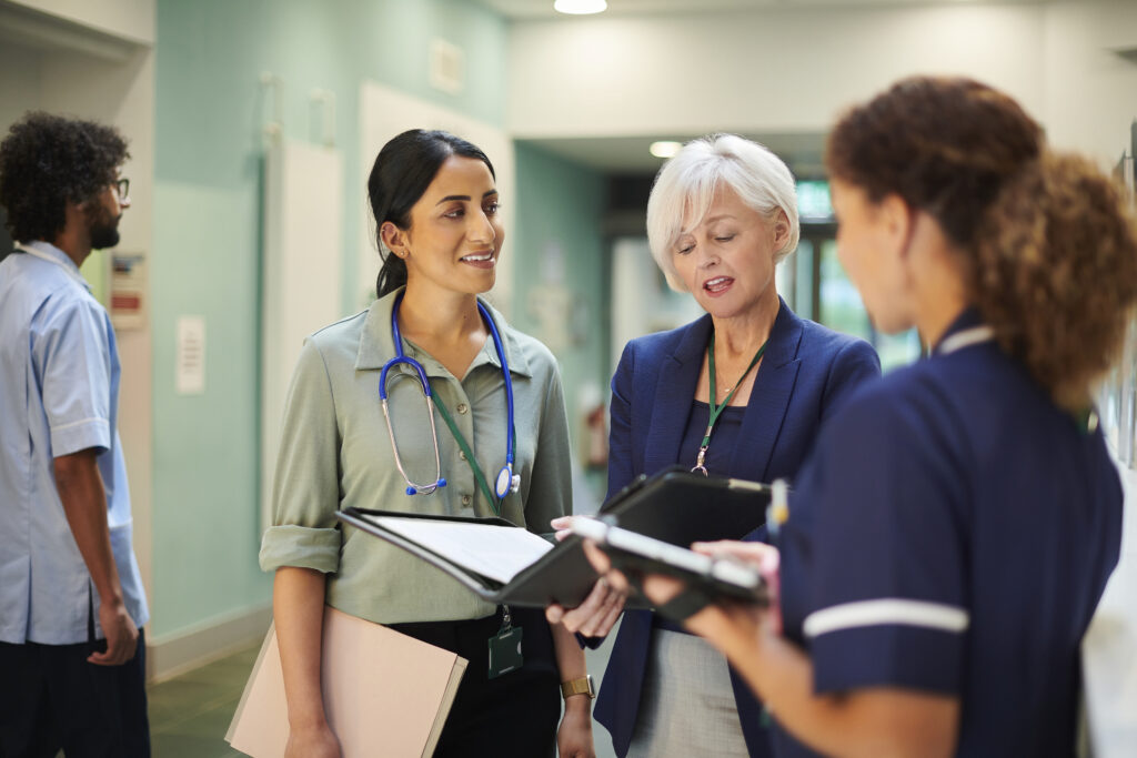 Diverse healthcare team of doctors and nurses collaborating in a hospital corridor, representing Guidehealth's integrated approach to supporting health systems and doctors.