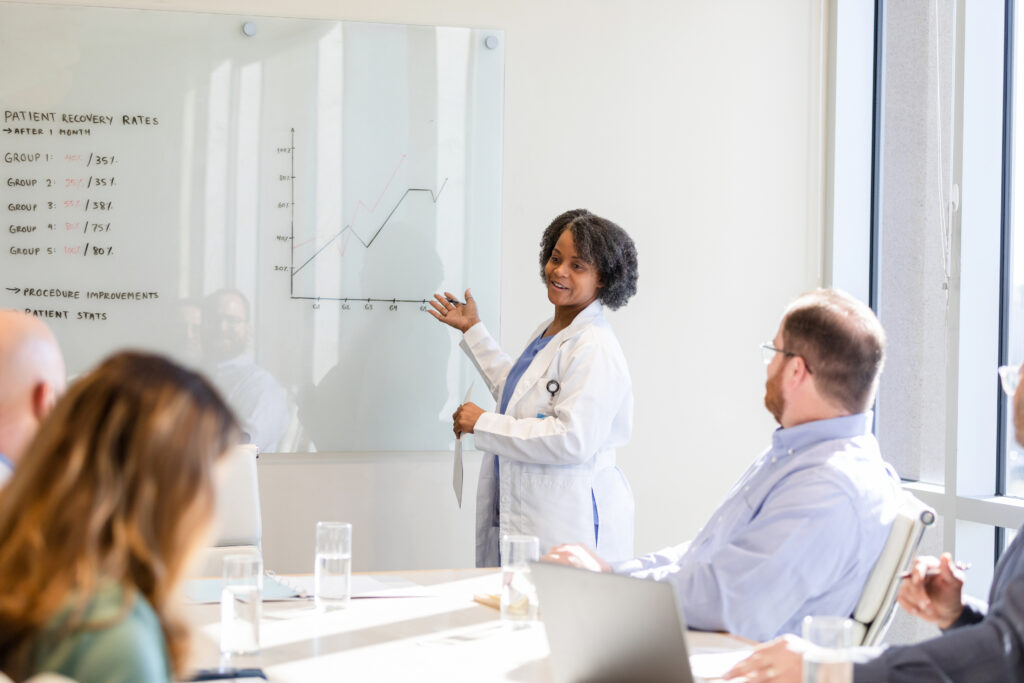 Healthcare provider presenting patient recovery rates and readmission trend data on a whiteboard to a clinical team, representing Guidehealth's data-driven approach to reducing hospital readmissions.